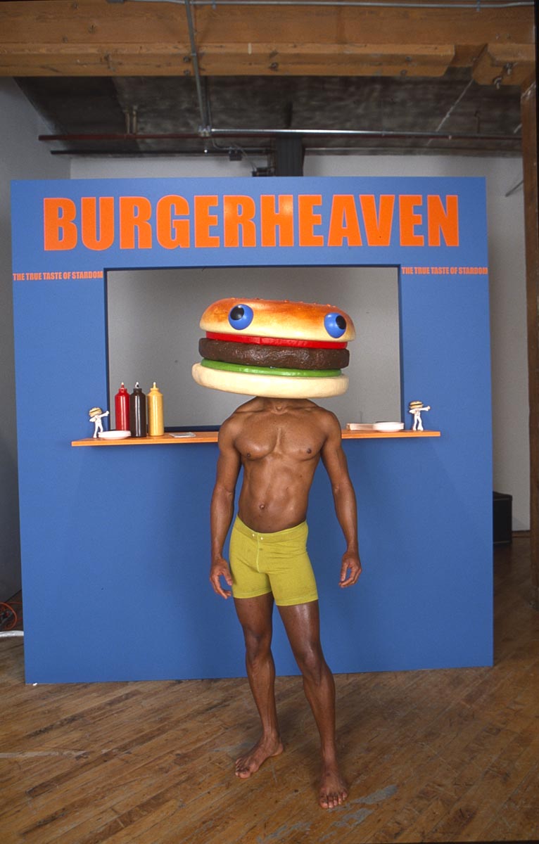 Burgerheaven: Installation View: Man modelling hamburger head, in fron of burger stand. Performance