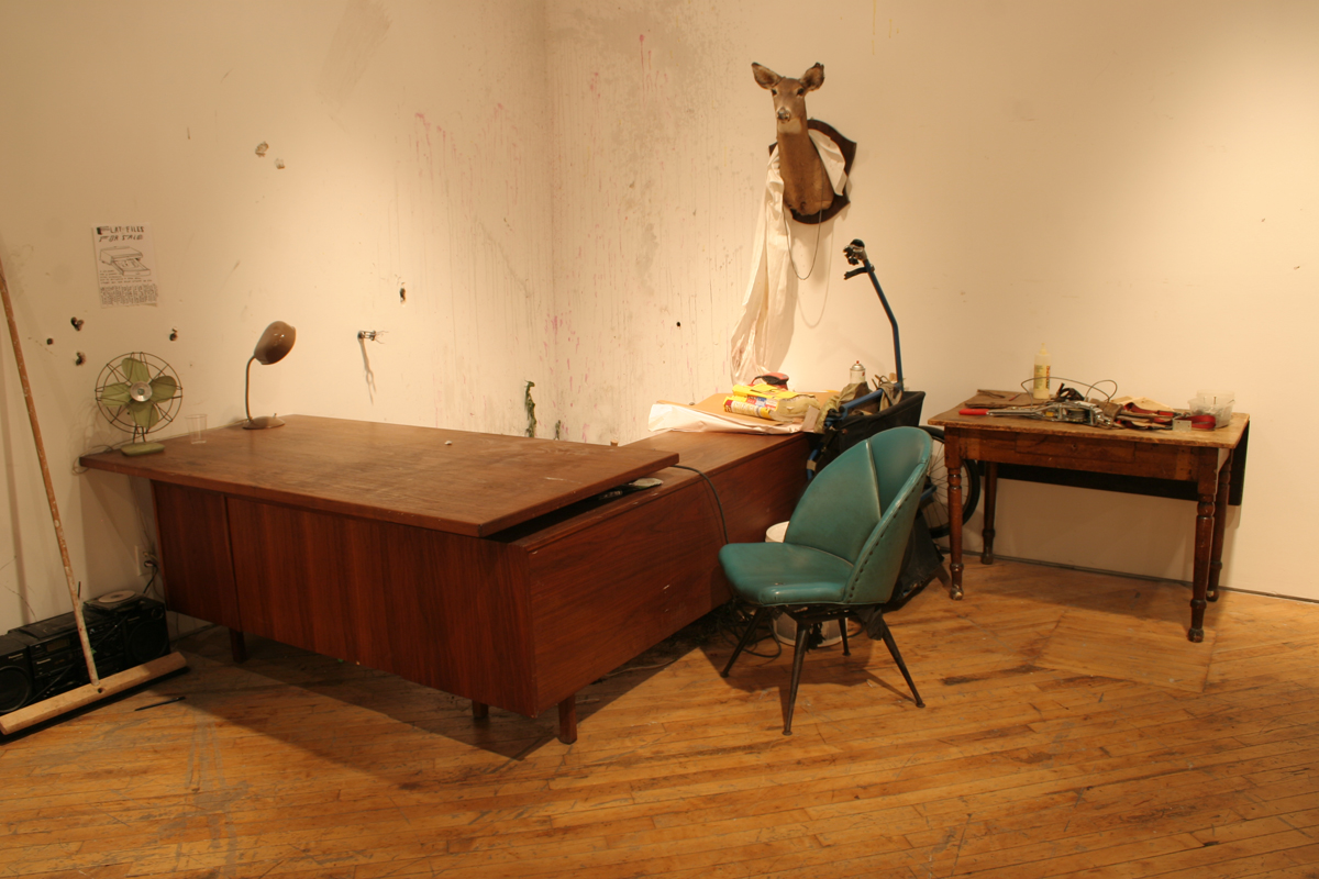 Swintak: Residency, image of a desk, green chair, taxidermy deer hung on wall.