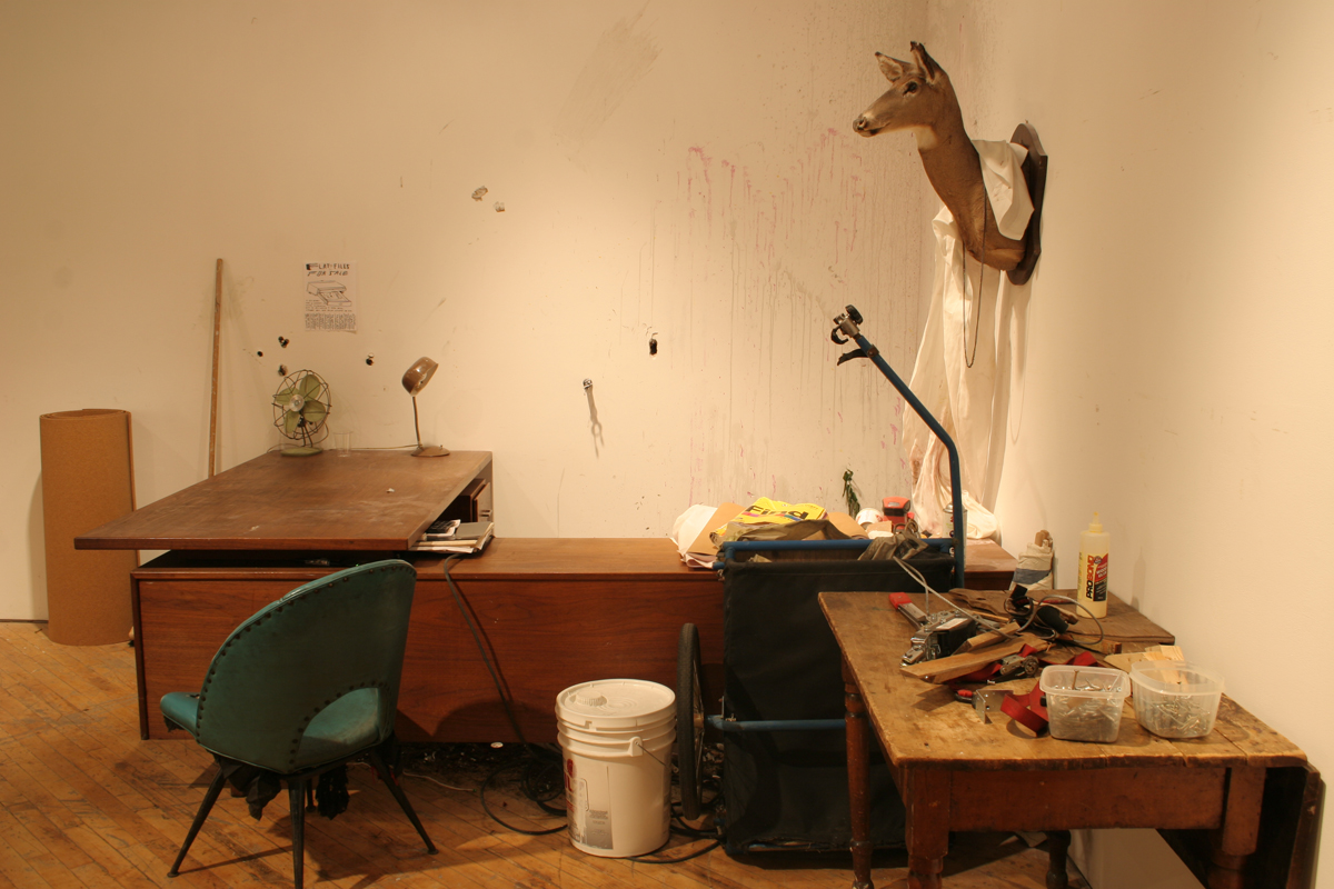 Swintak: Residency, image of a desk, green chair, taxidermy deer hung on wall.