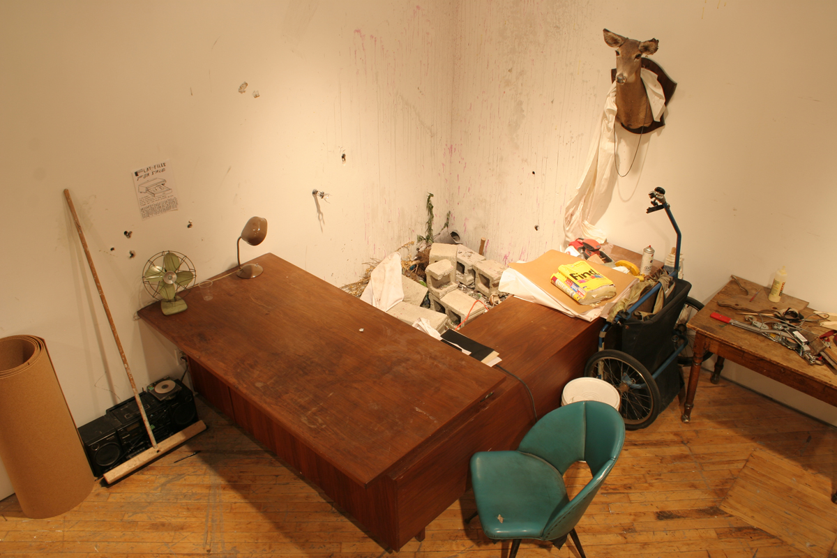 Swintak: Residency, image of a desk, green chair, taxidermy deer hung on wall.