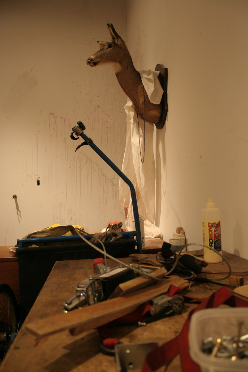 Swintak: Residency, image of a desk, green chair, taxidermy deer hung on wall.