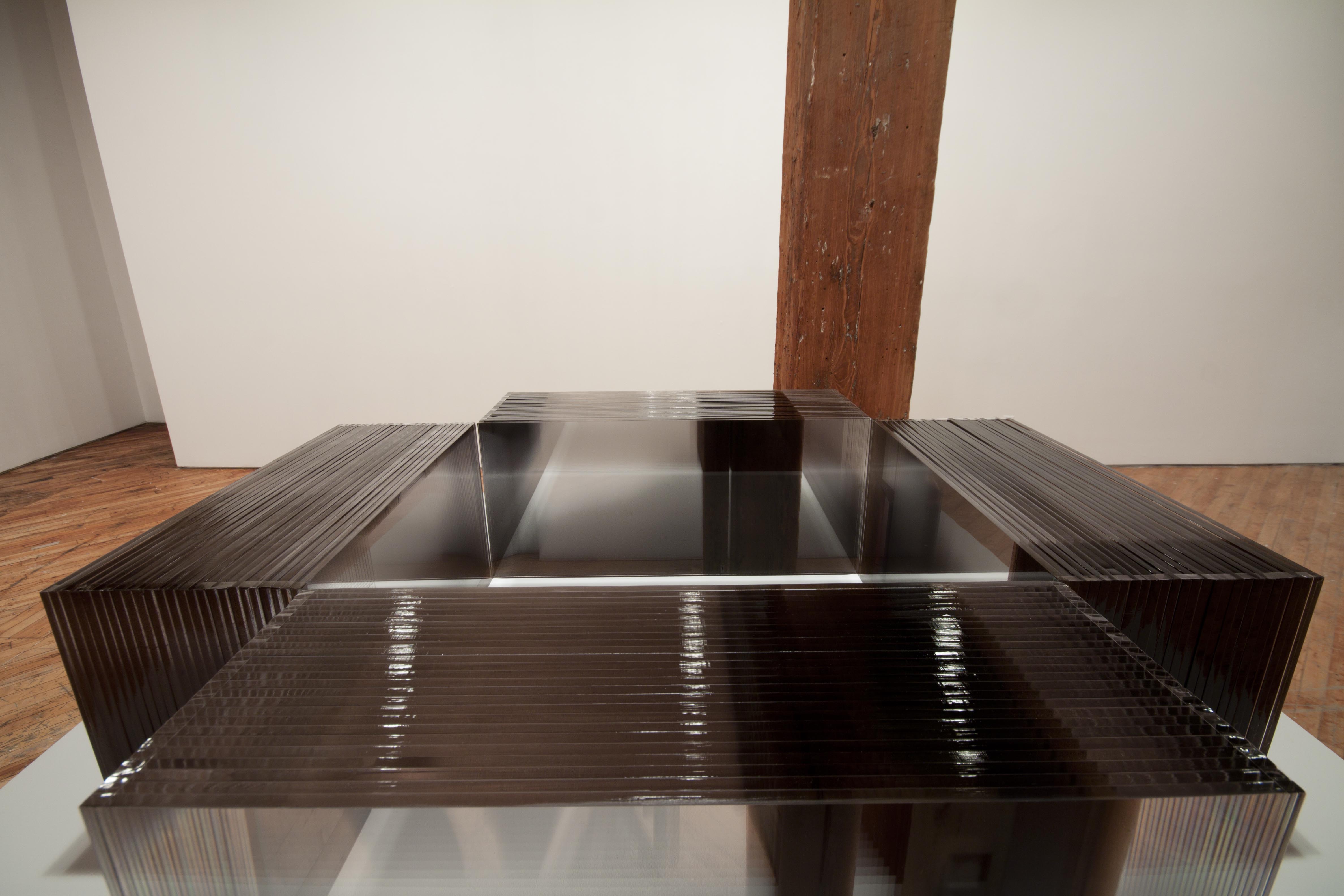KAREN HENDERSON, plinth, on top of which 4 acrylic rectangular blocks are placed so that each of their inside corners are touching. Each one is made up of 26 sheets of acrylic fused together. Each sheet has a photographic panorama printed on it a composite image of the gallery wall.