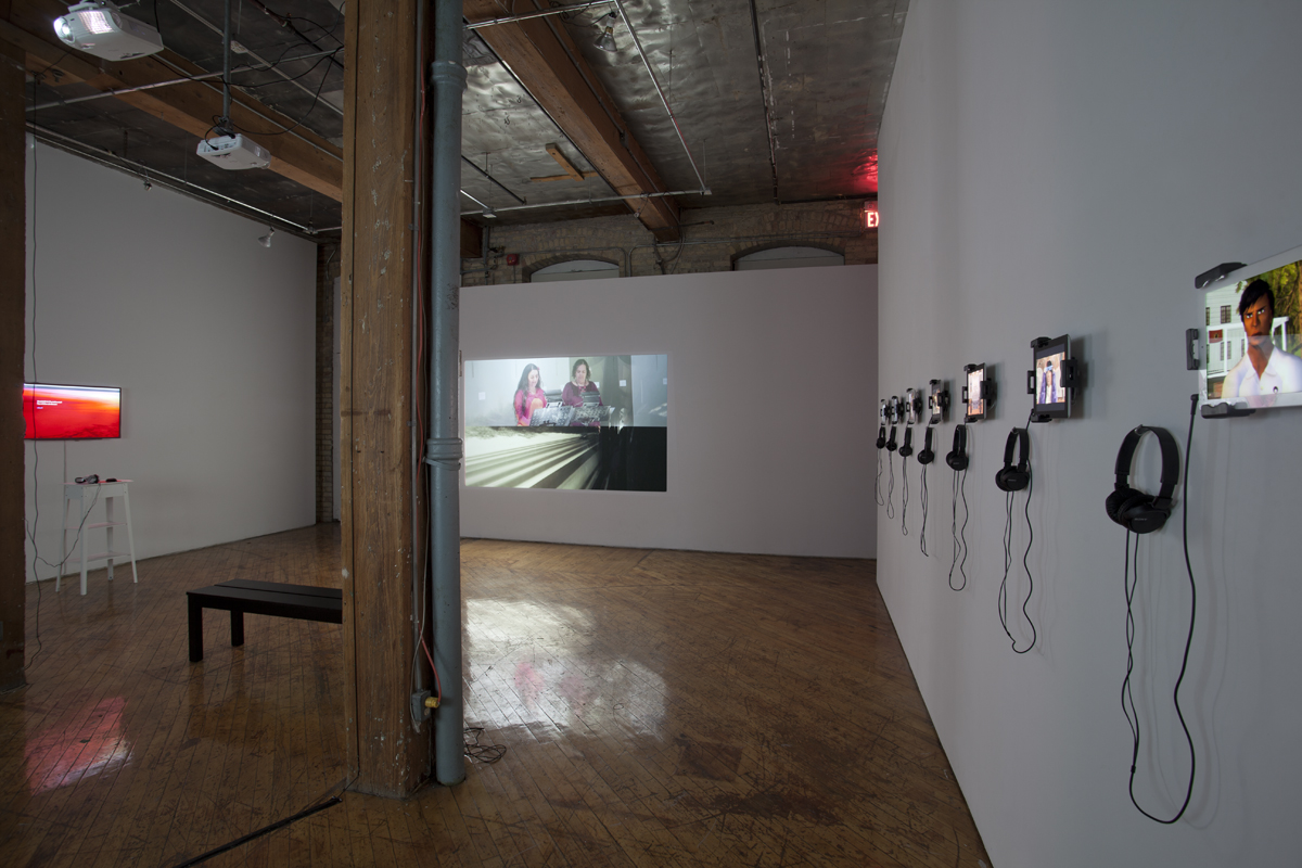 voz--voz/voice--voice provides a space for the articulation of different voices in the context of creative narratives and the frameworks enabled by new media and digital technologies, multiple small video monitors, projection on opposite wall.