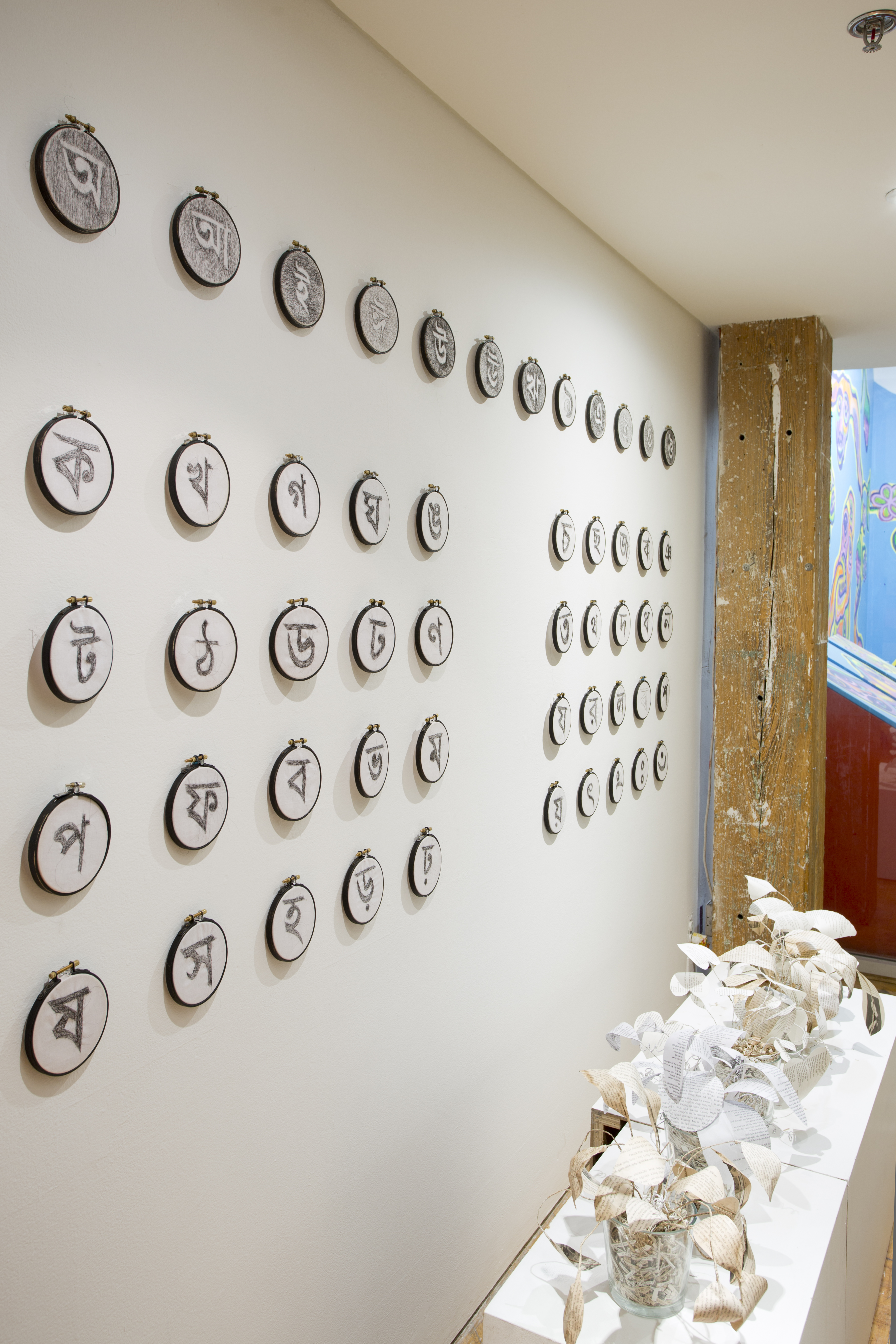 Asma Sultana, window installation, calligraphy symbols, created using hair crochet on mini circular canvases, displayed in rows.