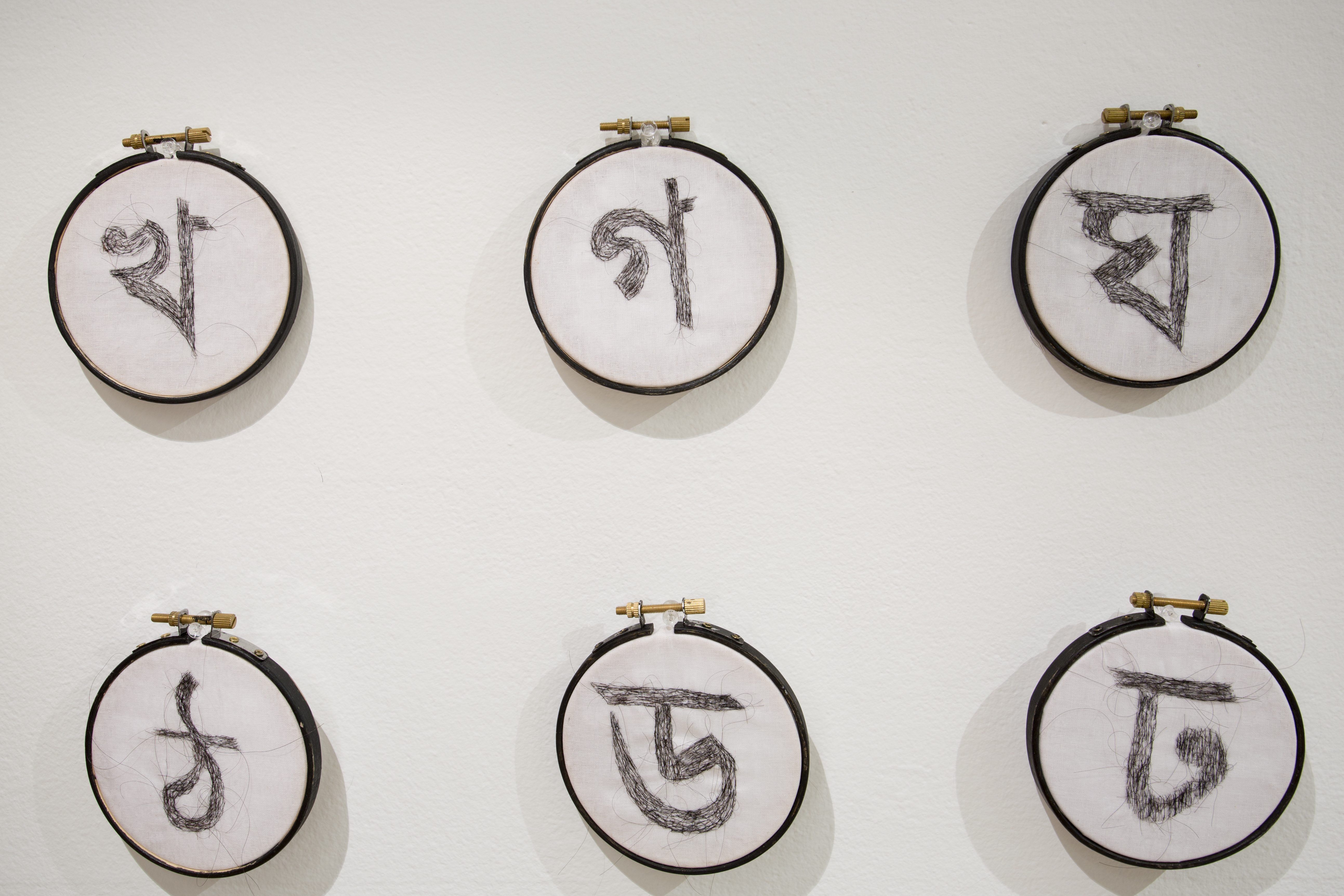Asma Sultana, window installation, calligraphy symbols, created using hair crochet on mini circular canvases, displayed in rows.