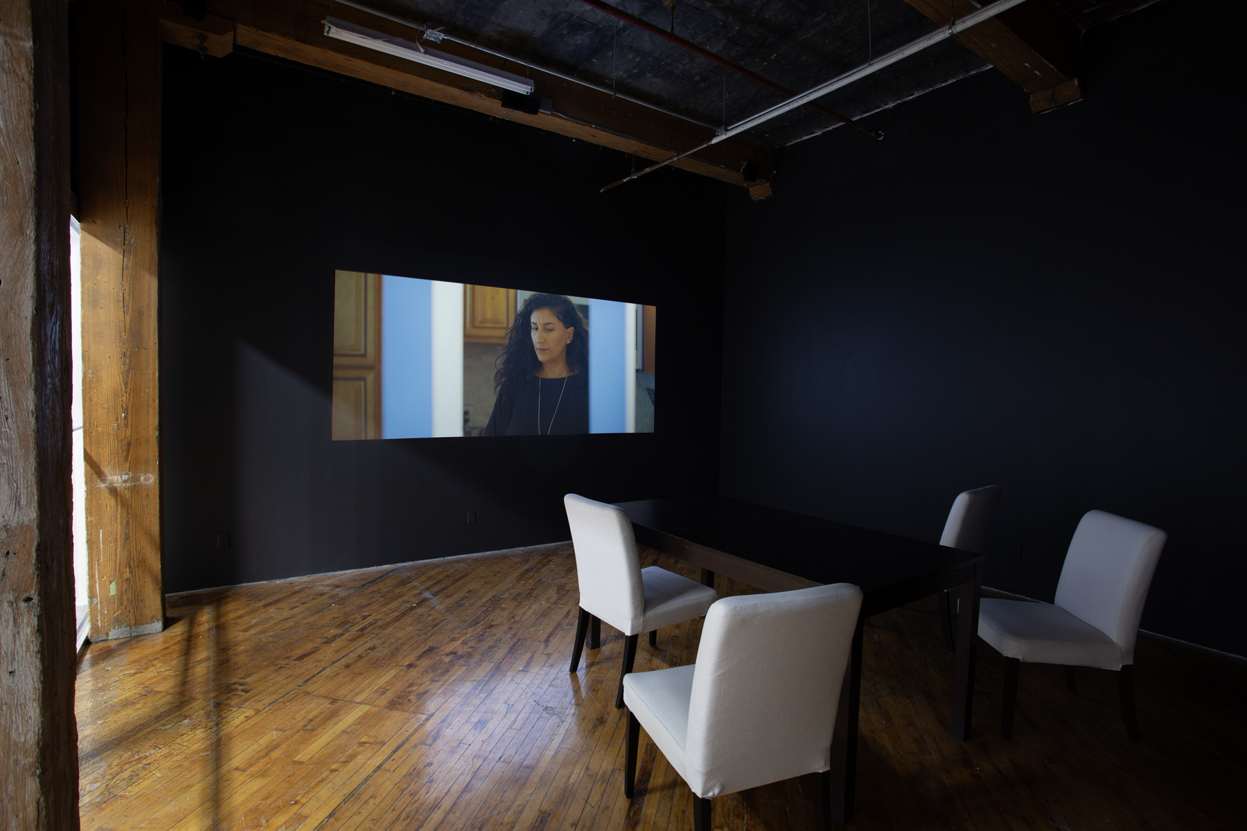 Zinnia Naqvi, view of installation, view of projection and table with chairs..