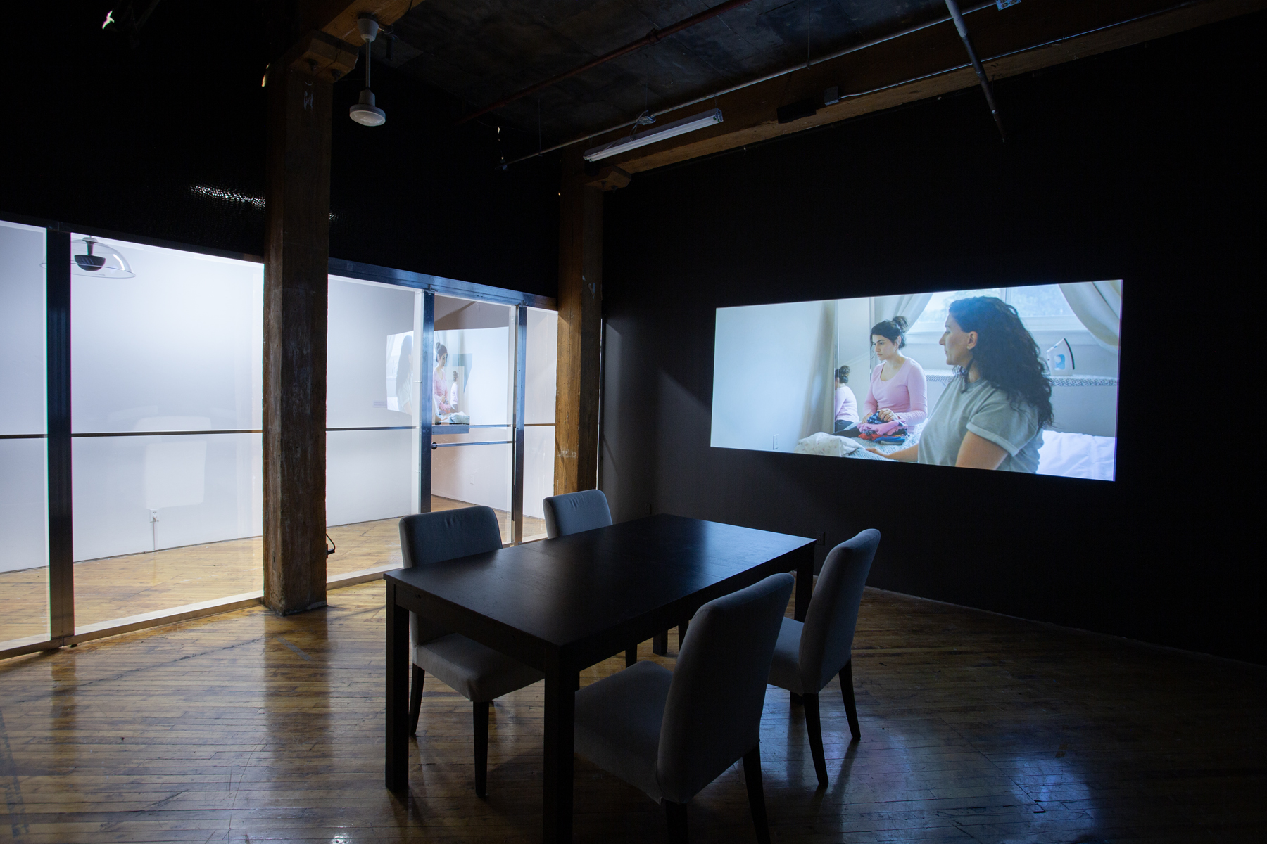 Zinnia Naqvi, view of installation, view of projection and table with chairs.