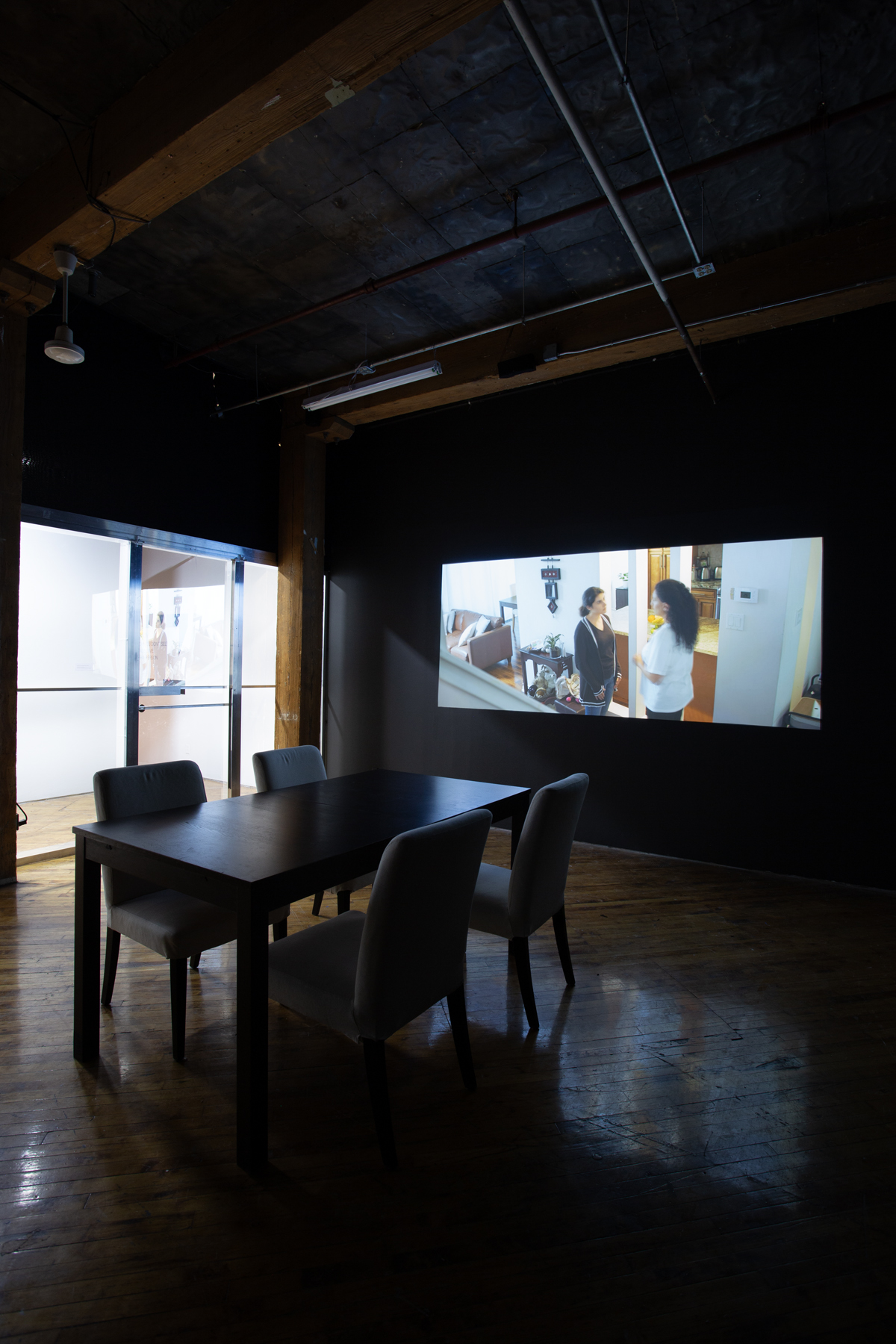 Zinnia Naqvi, view of installation, view of projection and table with chairs.