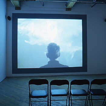 A room with a video art playing in front of chairs