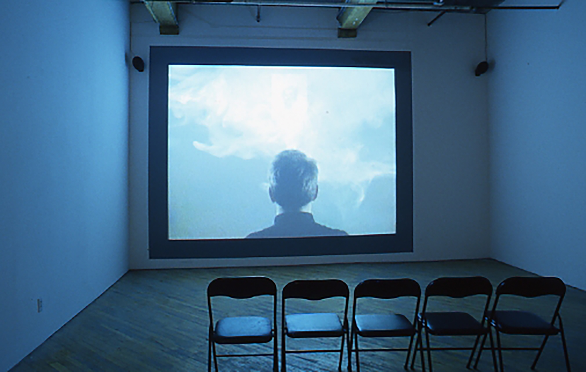 A room with a video art playing in front of chairs