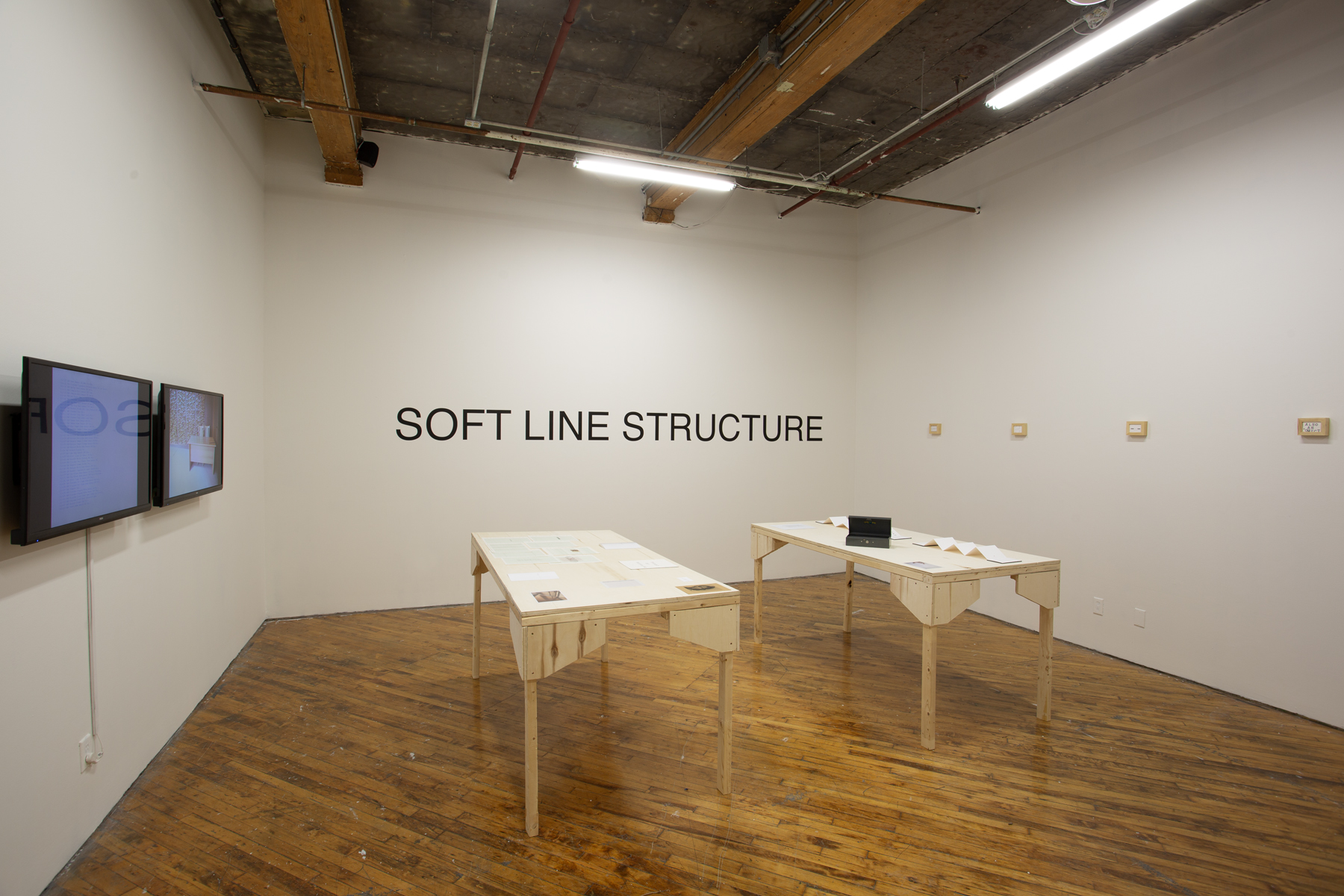 Yusuf Hassan, installation view, two tables arranged side by side, both contain printed material, and objects.