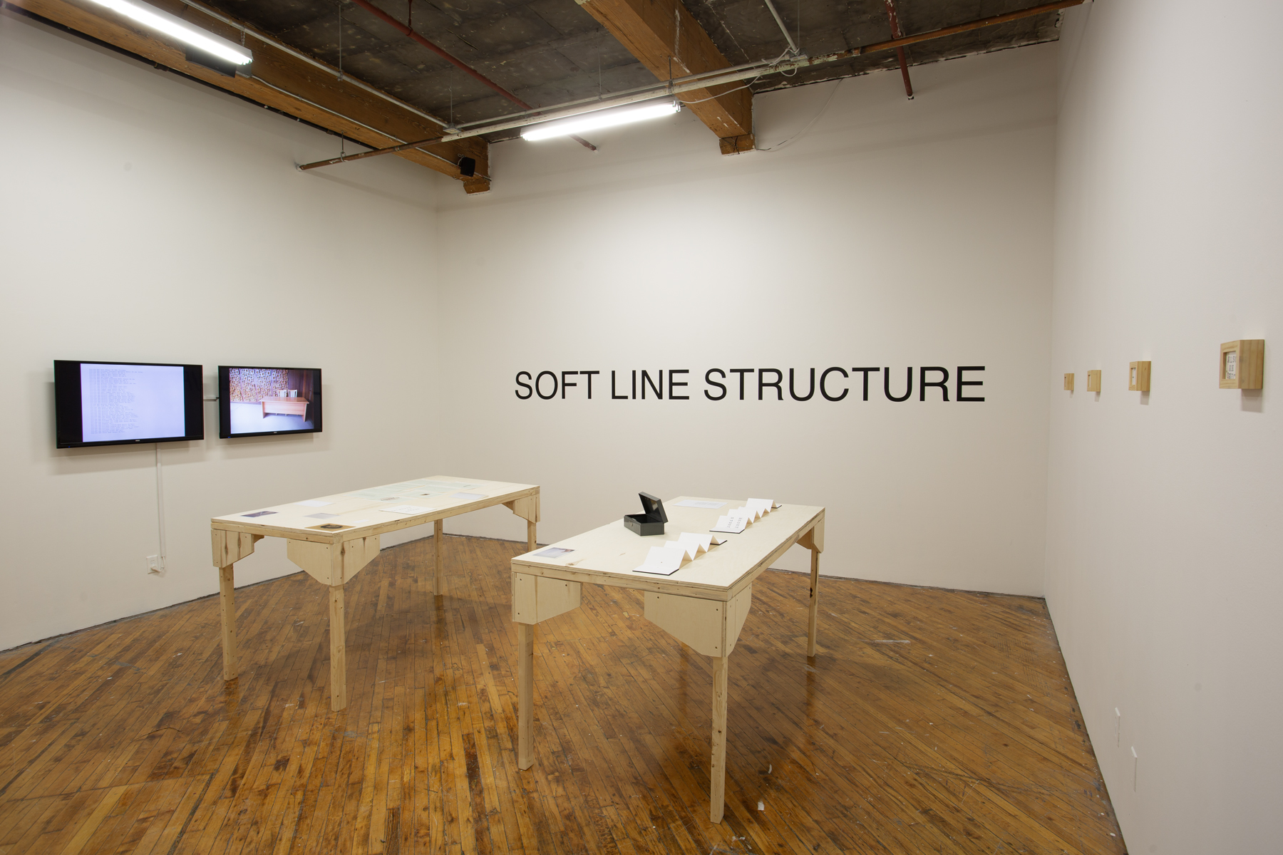 Yusuf Hassan, installation view, two tables arranged side by side, both contain printed material, and objects.