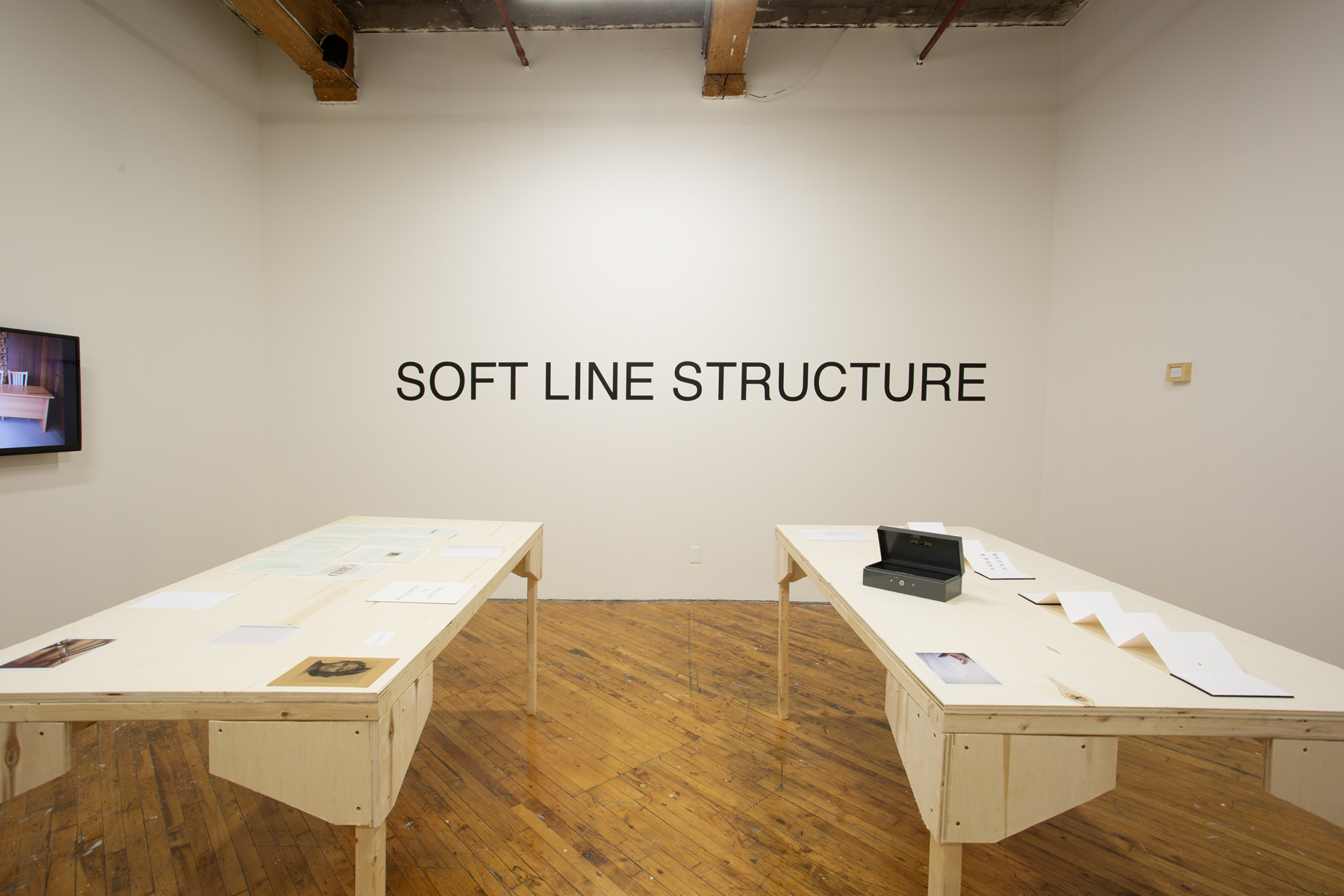 Yusuf Hassan, installation view, two tables arranged side by side, both contain printed material, and objects.