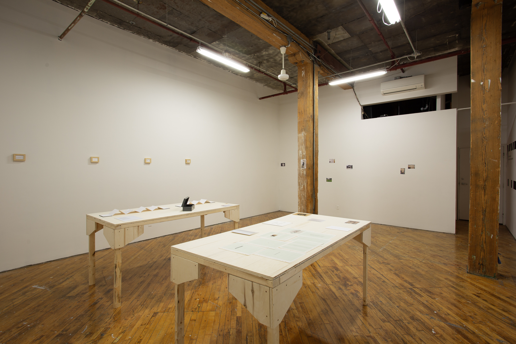 Yusuf Hassan, installation view, two tables arranged side by side, both contain printed material, and objects.