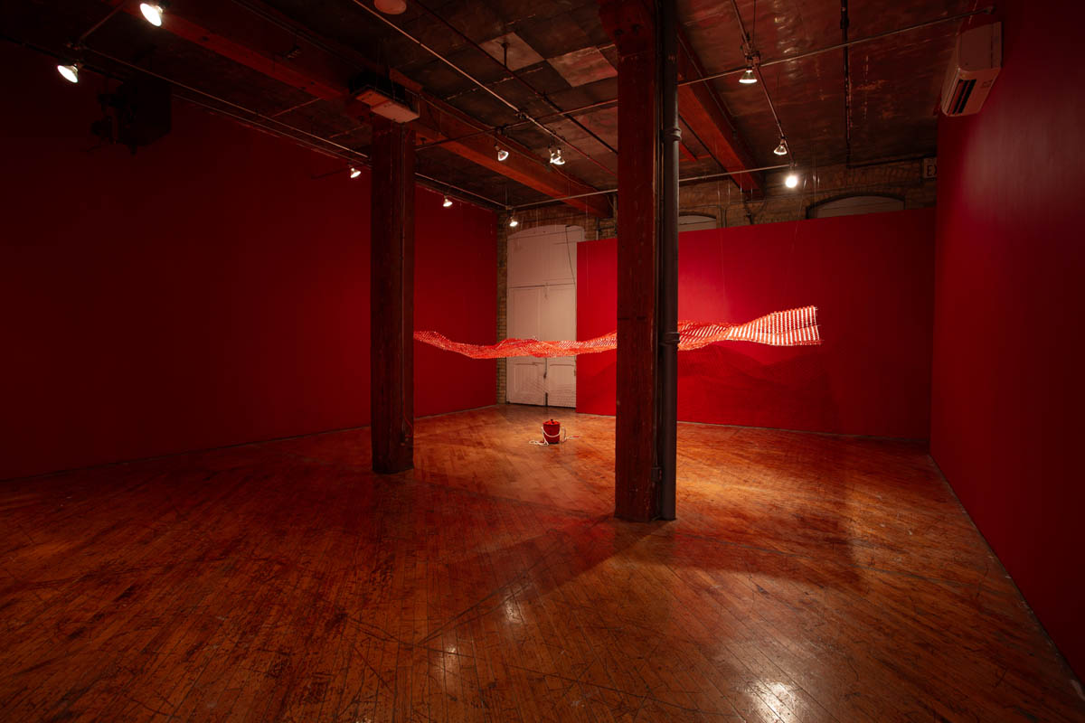Annie Wong: Installation view of large paper sculpture, hanging from the ceiling, gallery walls are painted red.