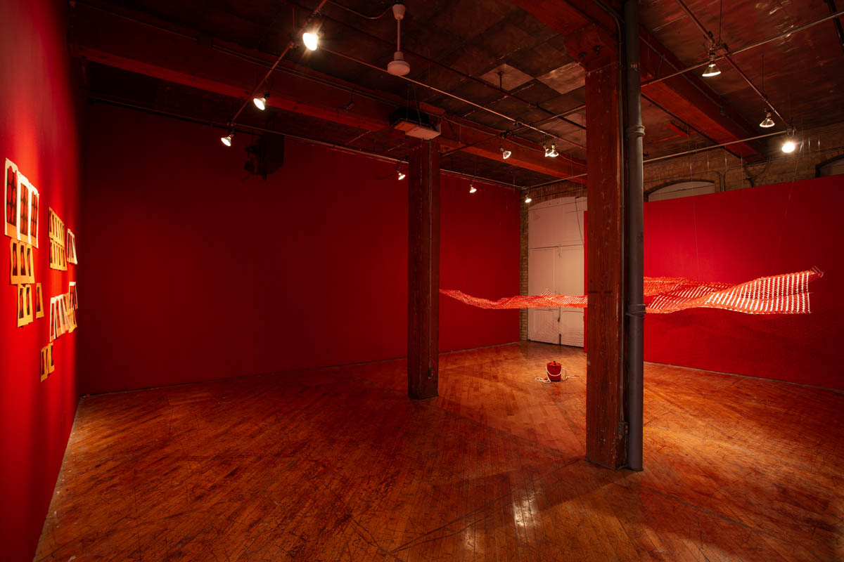 Annie Wong: Installation view of large paper sculpture, hanging from the ceiling, gallery walls are painted red.