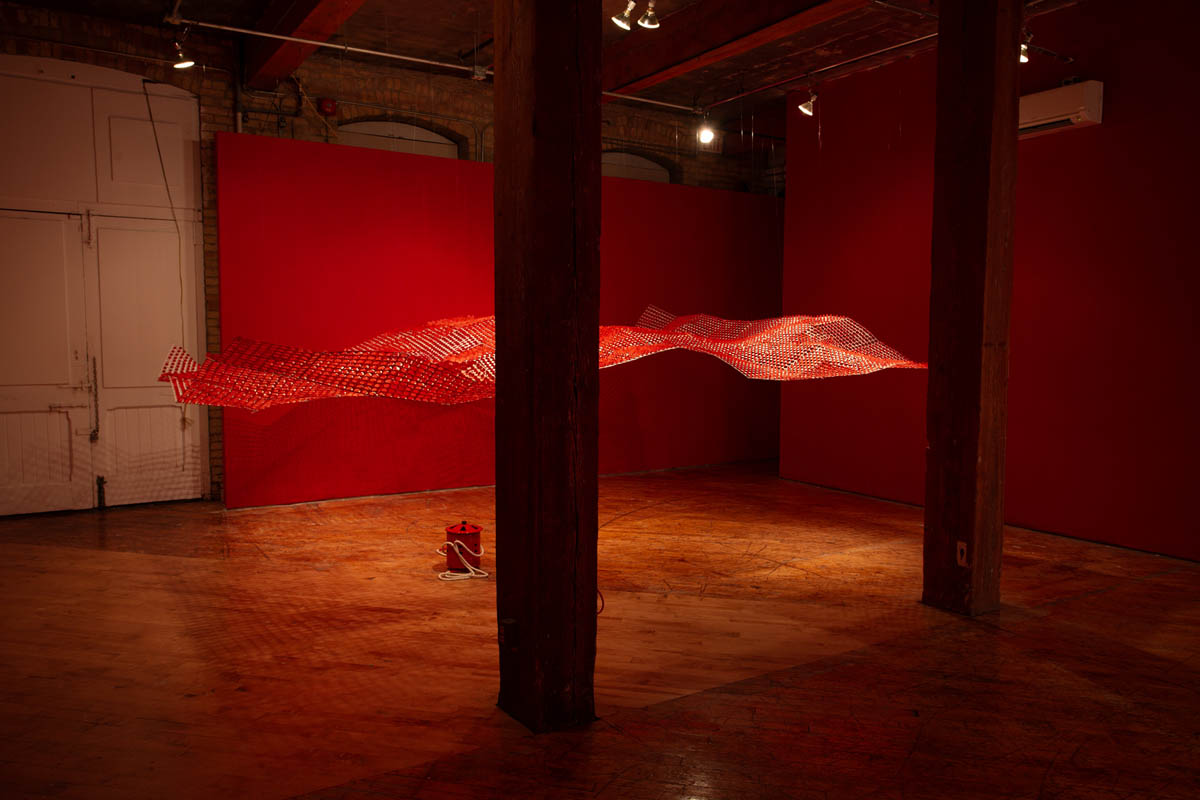 Annie Wong: Installation view of large paper sculpture, hanging from the ceiling, gallery walls are painted red.