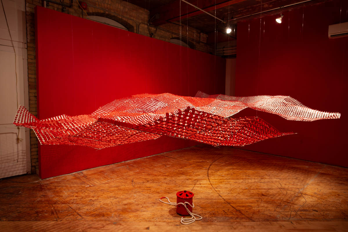 Annie Wong: Installation view of large paper sculpture, hanging from the ceiling, gallery walls are painted red.