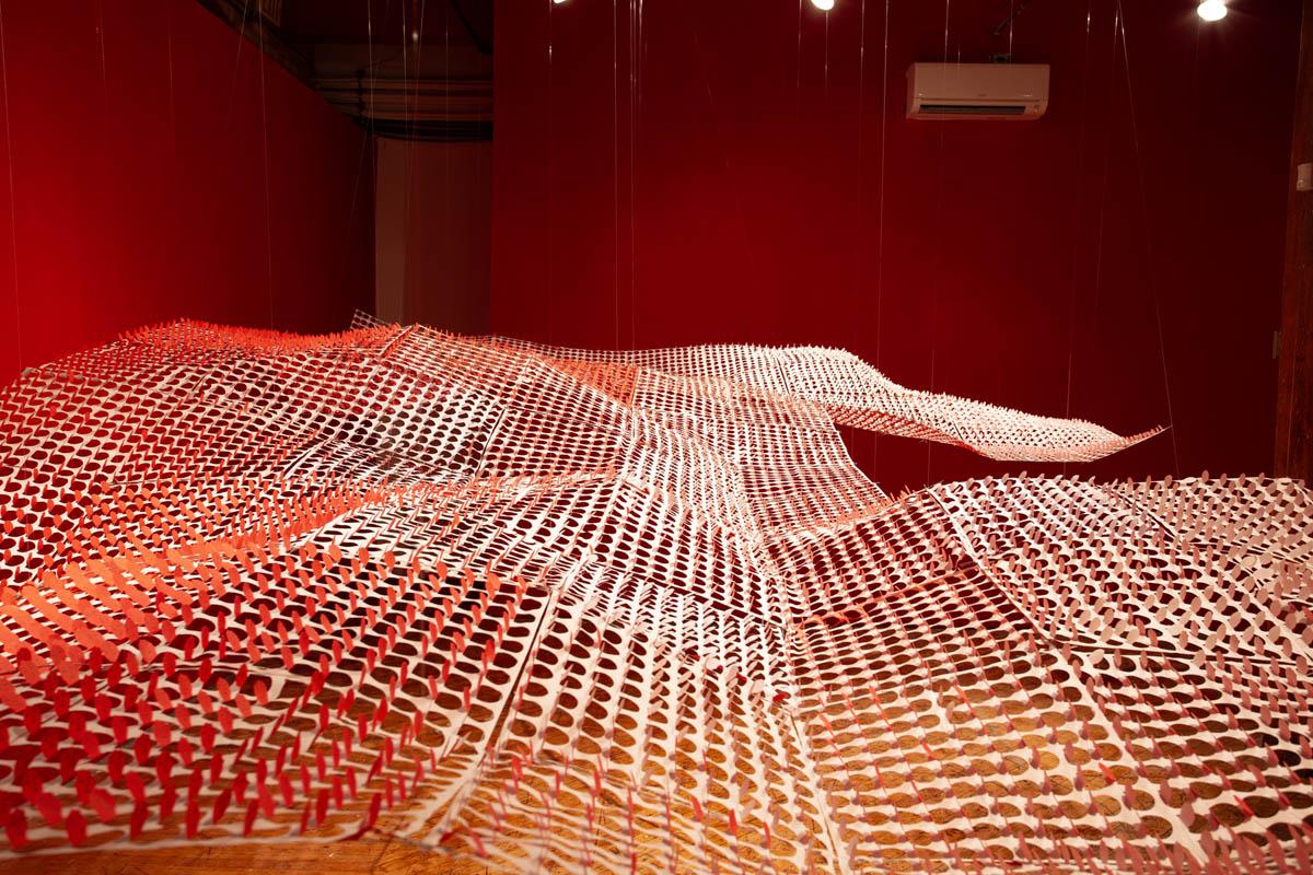 Annie Wong: Installation view of large paper sculpture, hanging from the ceiling, gallery walls are painted red.