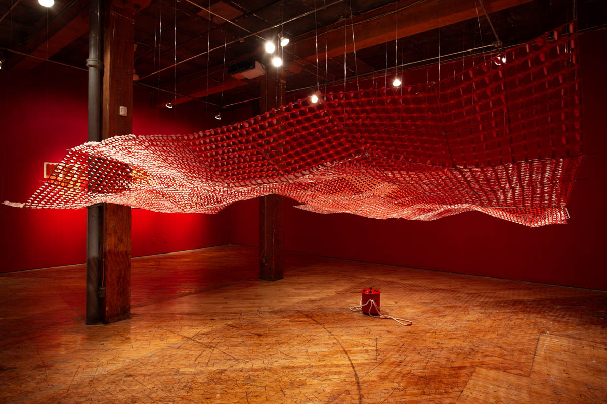 Annie Wong: Installation view of large paper sculpture, hanging from the ceiling, gallery walls are painted red.