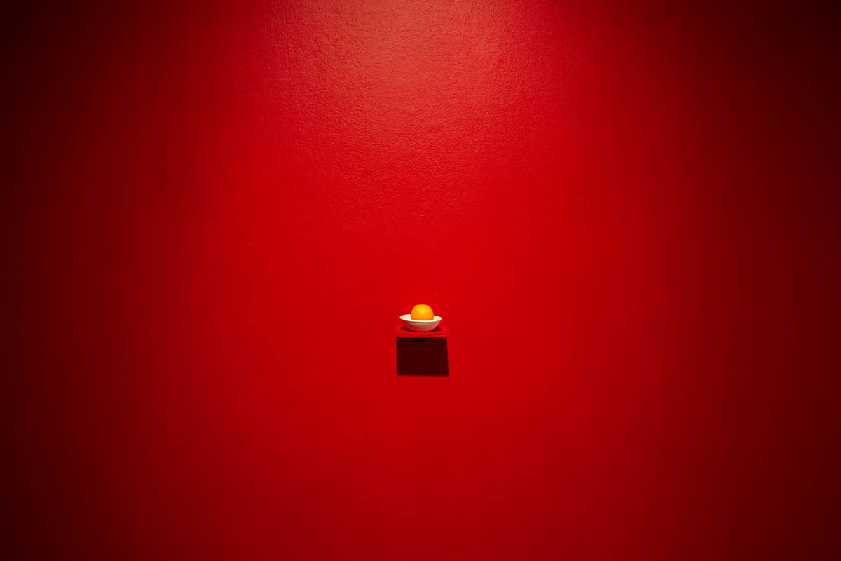 Annie Wong: Installation view, detail of an orange displayed on a shelf, the gallery walls are red.