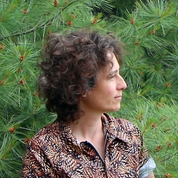 Person with short brown wavy hair, in profile against greenery.