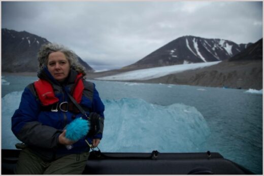 Woman in lifejacket sits on boat with snowy mountains in the horizen